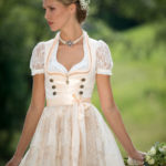 Frau in beigem Dirndl mit Blumenstrauß in der Hand